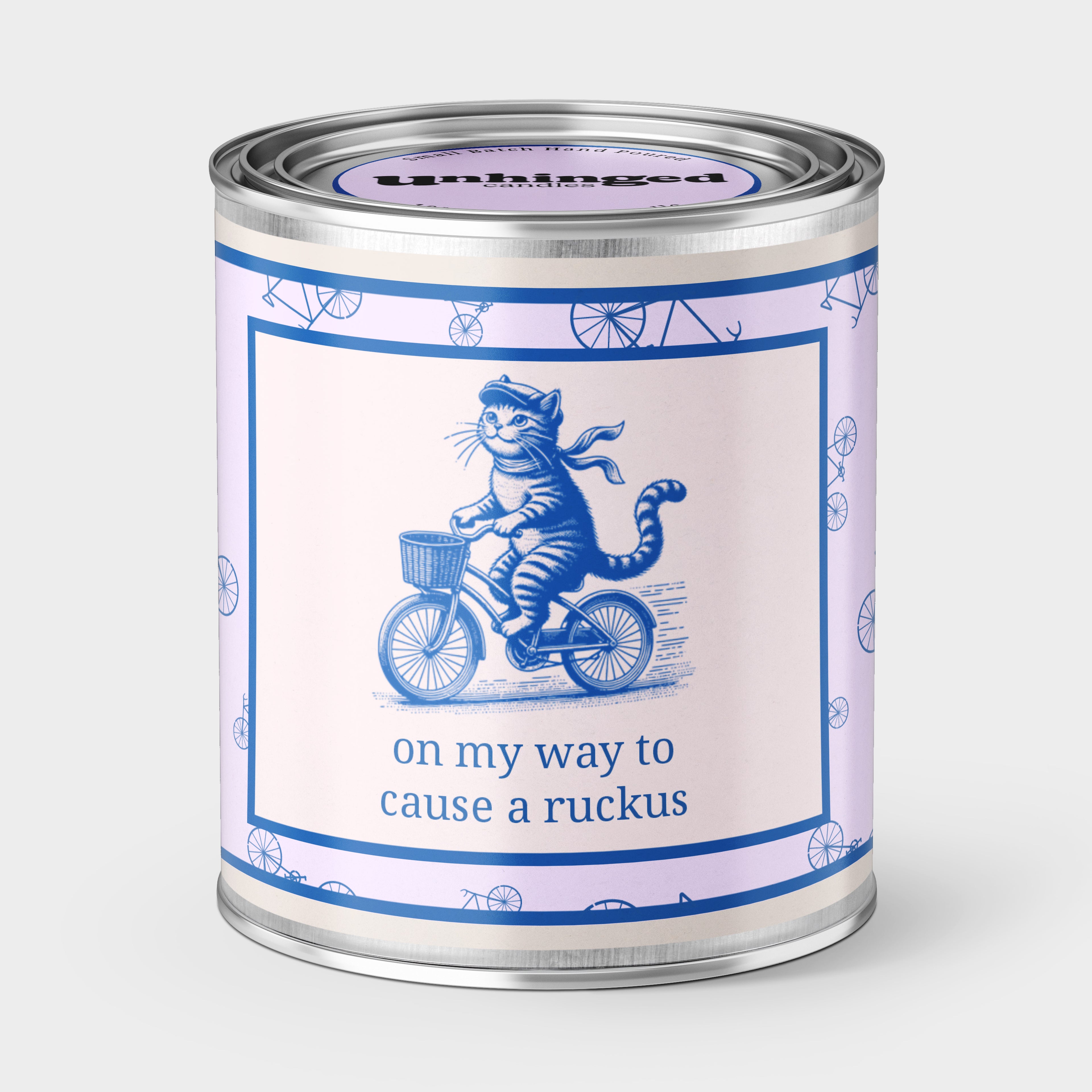 An Unhinged Paintcan candle with a picture of a happy cat riding a bike with the phrase "on my way to cause a ruckus" printed on it. 